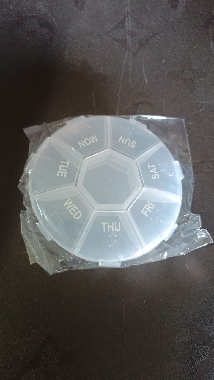 A clear 7-day pill organizer, still in its plastic packaging, on a dark surface.