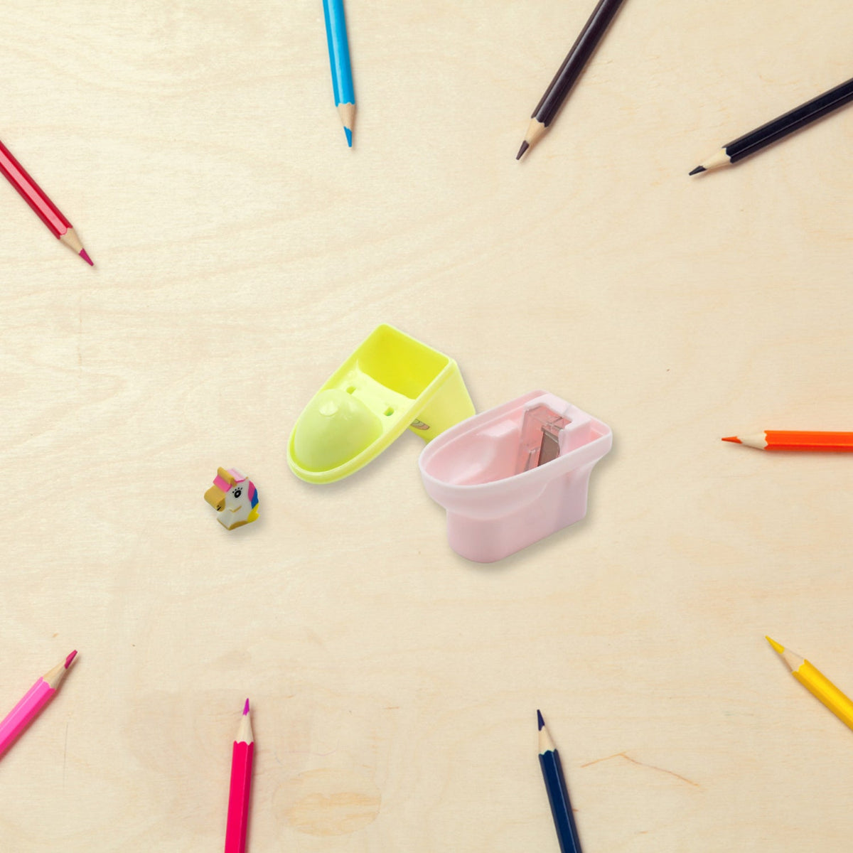 A disassembled pastel yellow and pink toilet-shaped pencil sharpener and a small unicorn eraser are on a light wooden