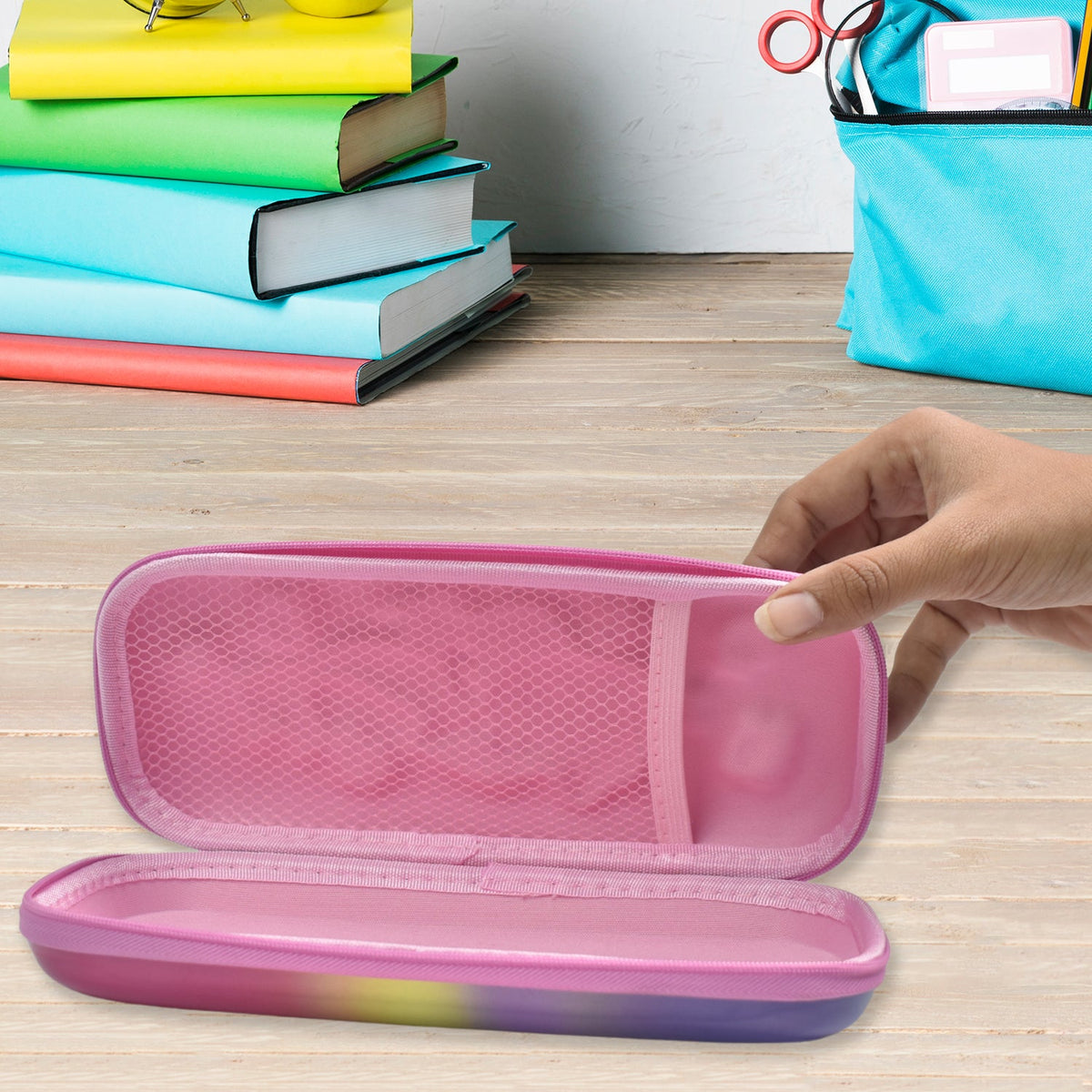 A hand opening the pink interior of a mermaid pencil case, revealing a mesh pocket, with school supplies in the background.