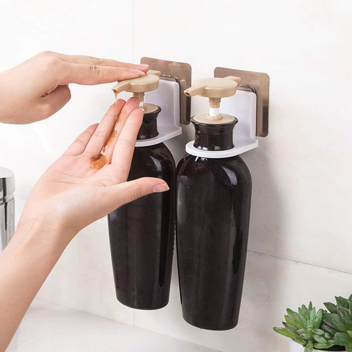 A person dispenses brown liquid from a dark brown bottle in a wall-mounted holder, next to another dark brown bottle.