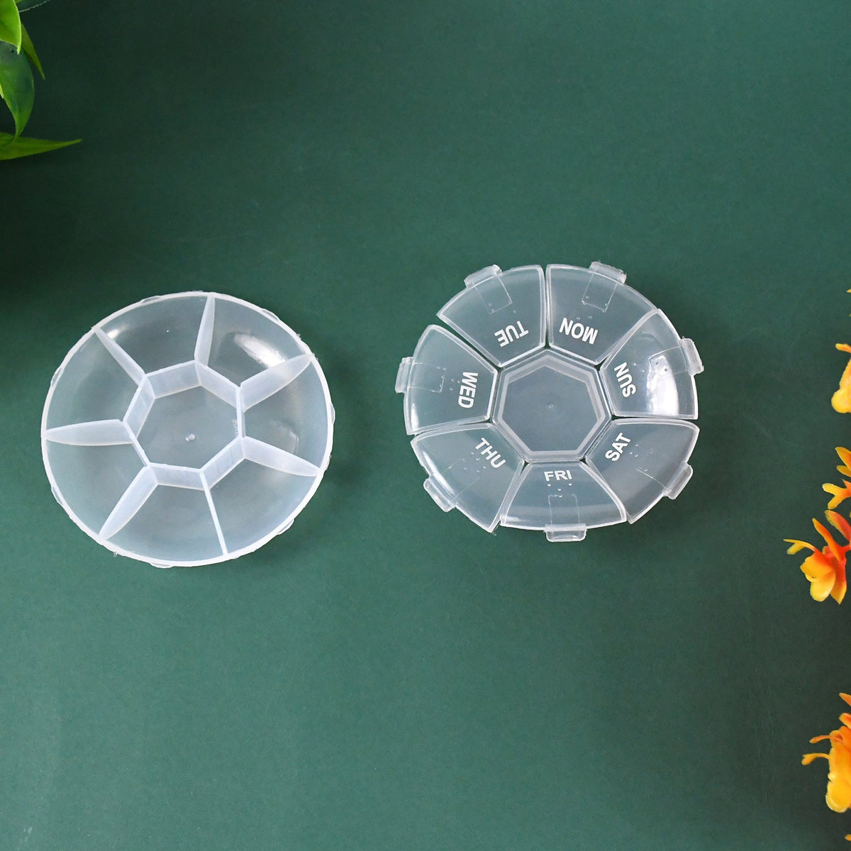 Two clear 7-day pill organizers, one assembled and one disassembled, on a dark green surface.