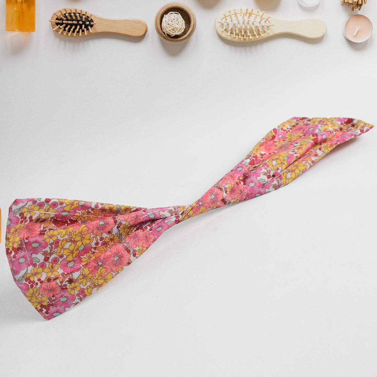 Pink and yellow knotted wire headband laid flat on a white surface with various hairbrushes.