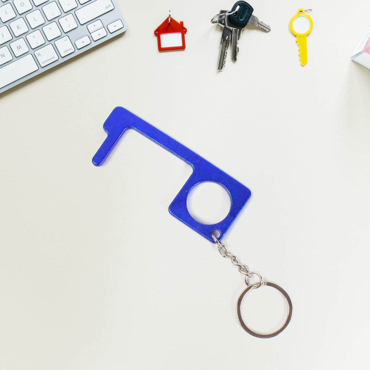 Hand holding Safe Touch Tool metal keychain used for touch-free door opening