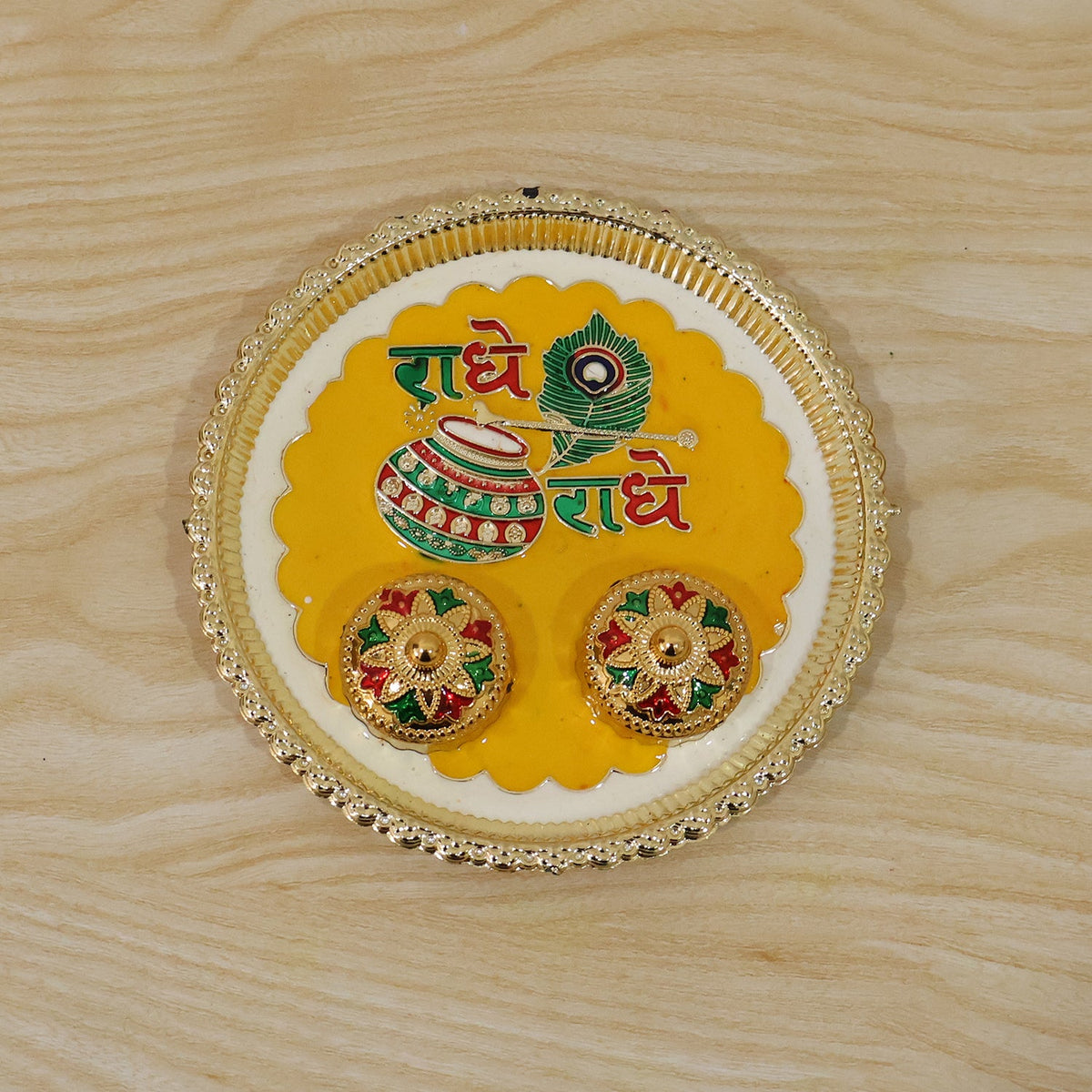 A silver and yellow Radhe Radhe pooja thali set with two small decorative containers on a light wooden background.