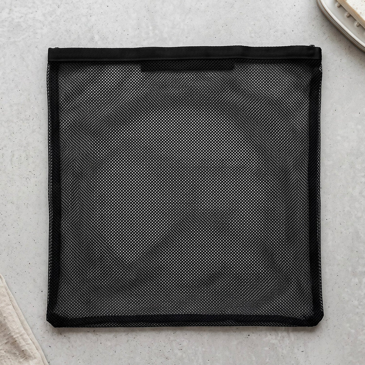A flat black mesh zipper storage bag is laid out on a light grey textured surface.