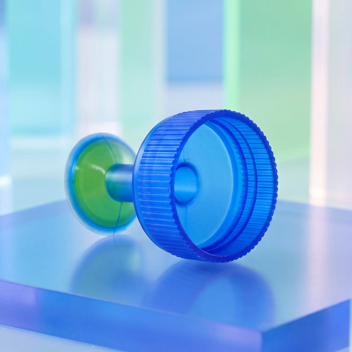 The blue and green plastic sprinkler cap lies on its side on a blue translucent block, showing the threaded underside.