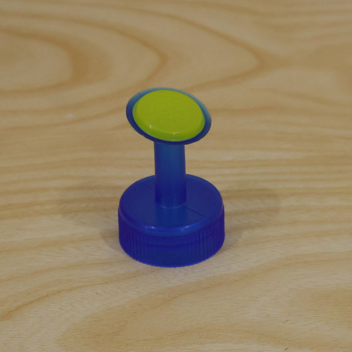 A blue and green plastic sprinkler cap stands on a light wooden surface.