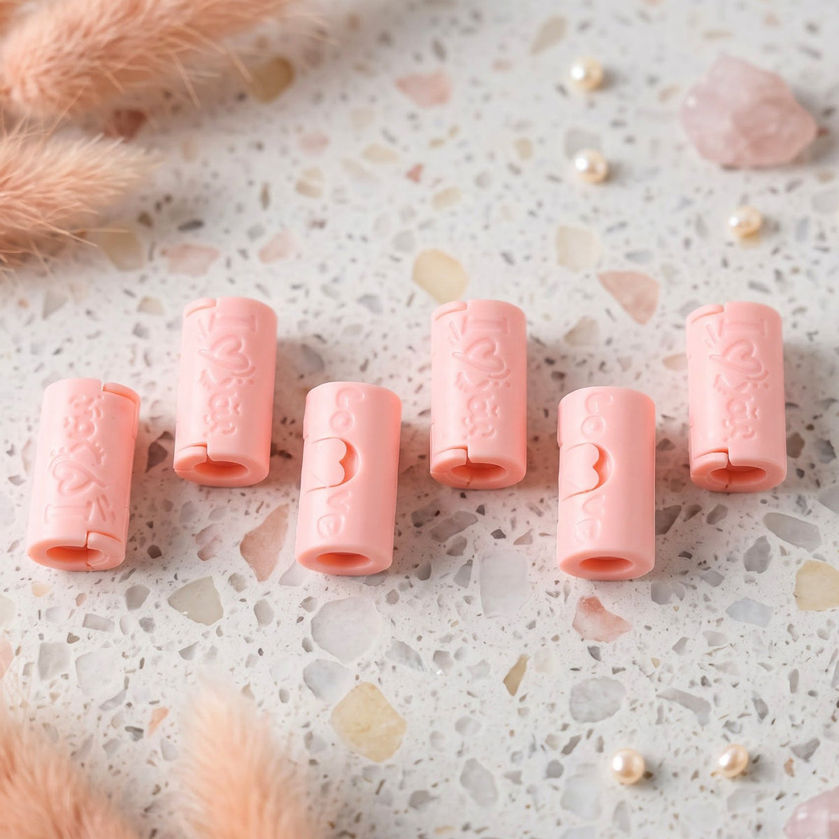 Six pink plastic bed sheet clips arranged on a speckled white and grey surface, surrounded by decorative elements.