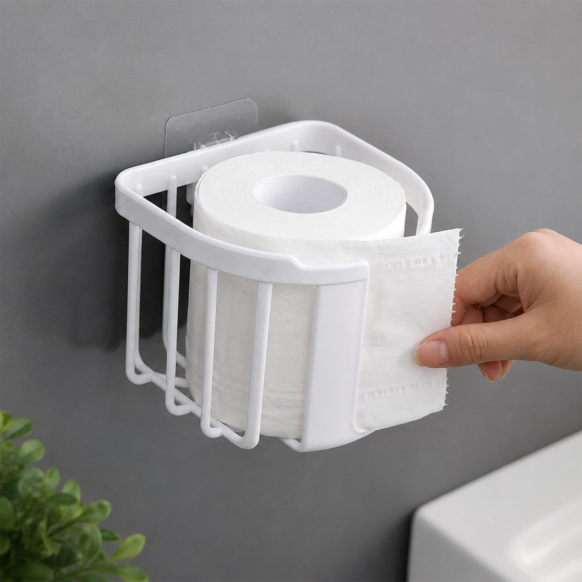 A hand tears a sheet from a roll of toilet paper held in a white plastic holder mounted on a gray wall.