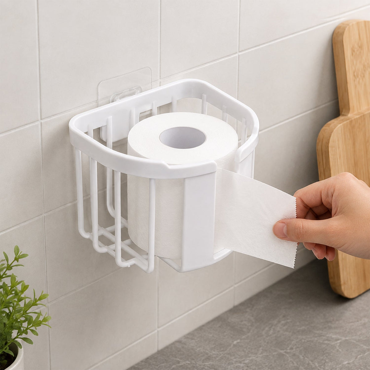 A white plastic toilet paper holder on a tiled wall holds a roll of toilet paper as a hand tears a sheet, with a cutting