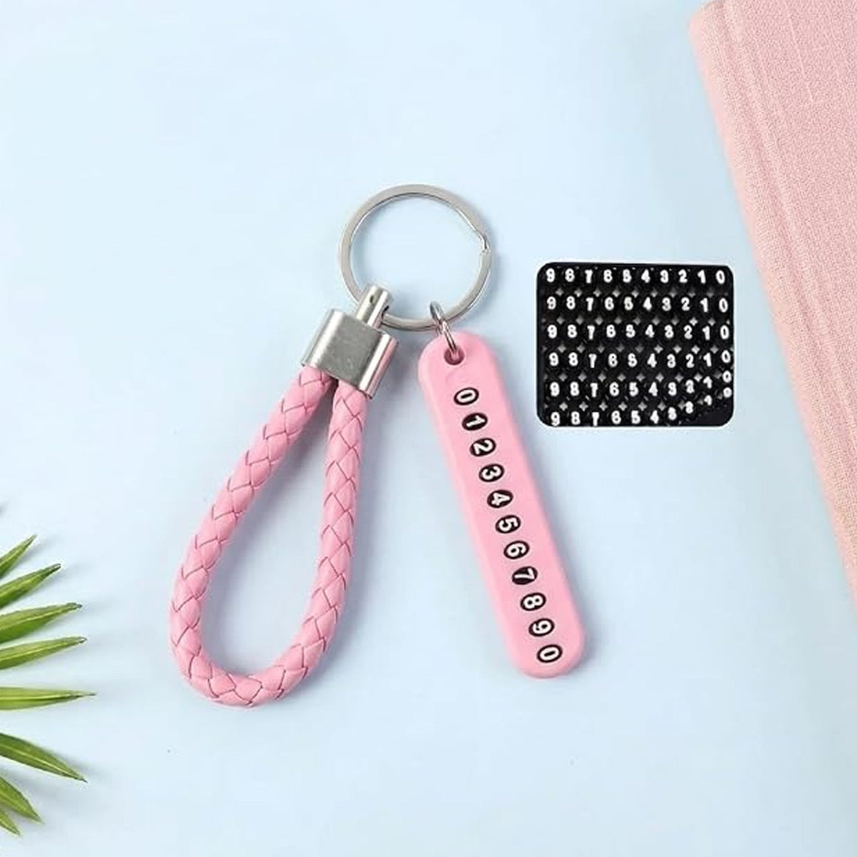 A pink braided wrist loop keychain with a pink number tag and a sheet of number stickers on a light blue surface.