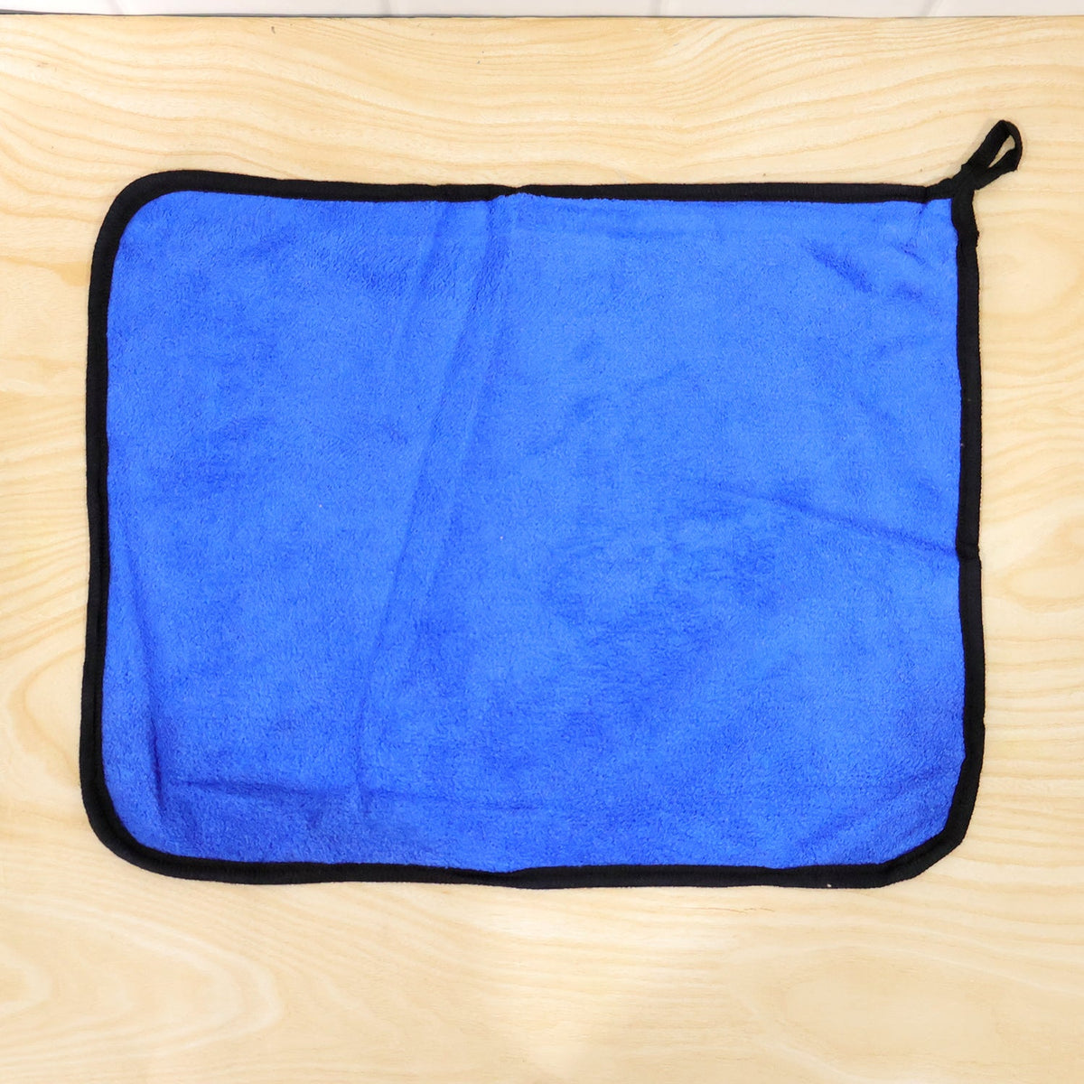 A blue microfiber cleaning cloth with a black border lies flat on a light wooden surface.