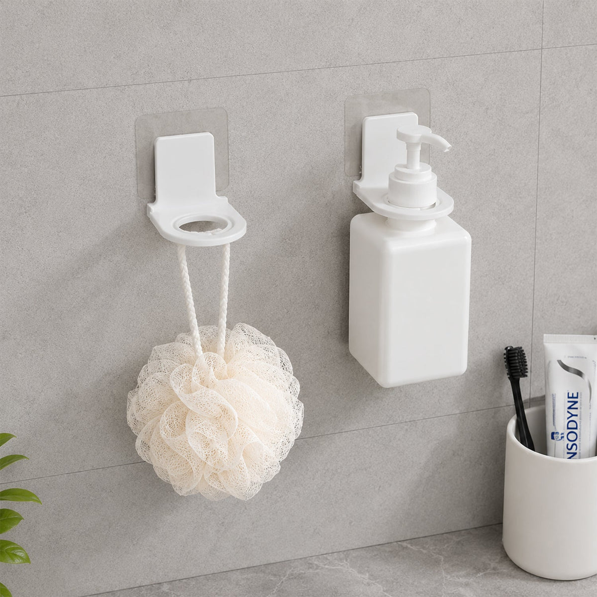 Product box for wall-mounted dispenser holders, alongside two white plastic holders and their clear adhesive pads on a