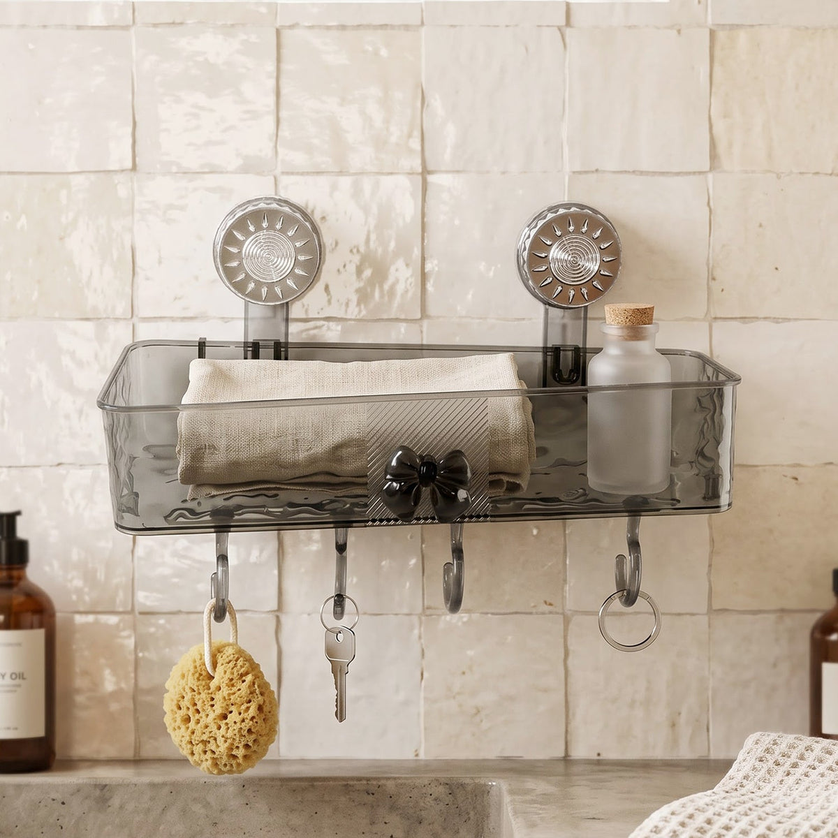 A clear grey plastic caddy with four hooks is mounted on a textured white wall, holding a sponge, keys, and a small bottle.