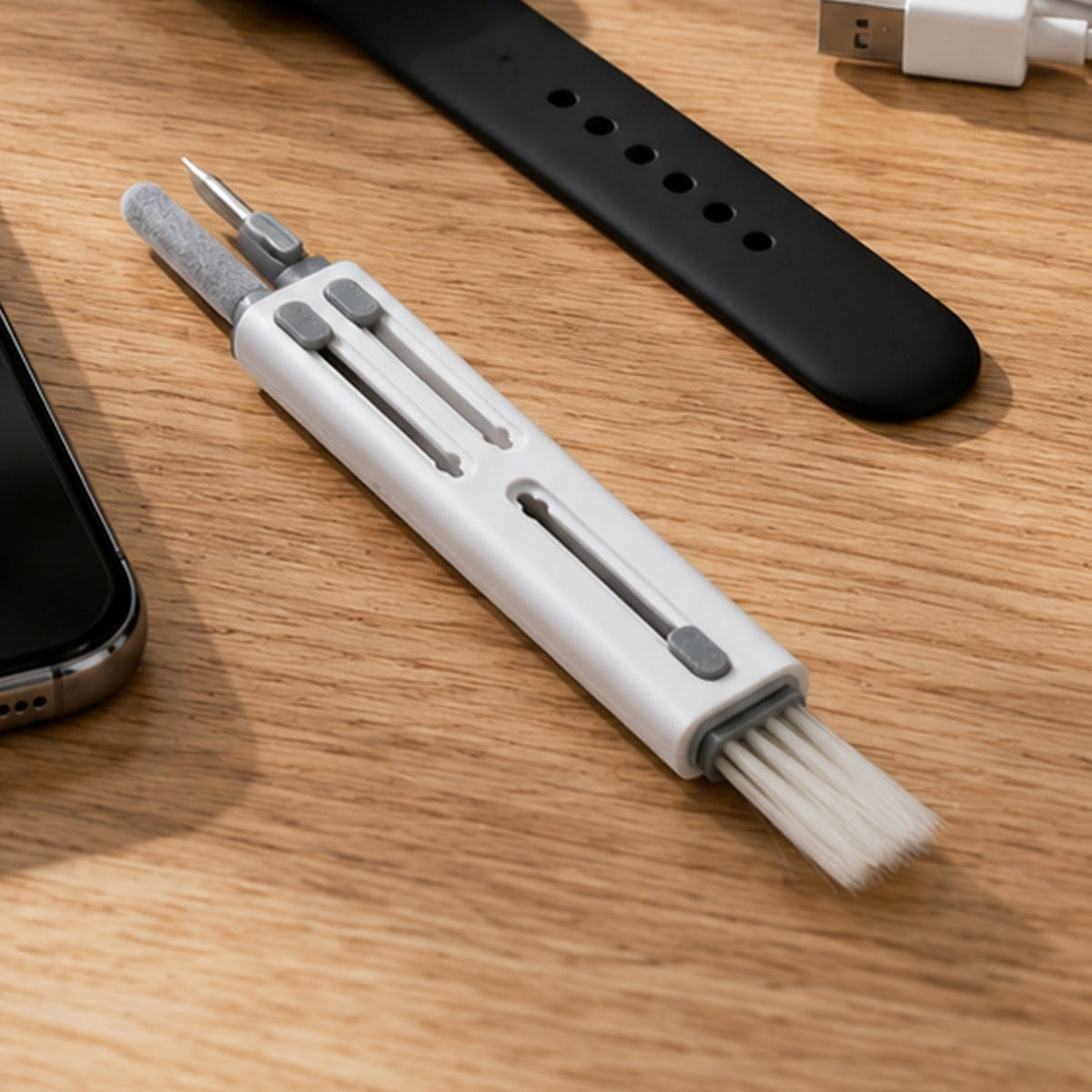White and gray multi-tool cleaning pen on a wooden desk next to a phone and watch strap.