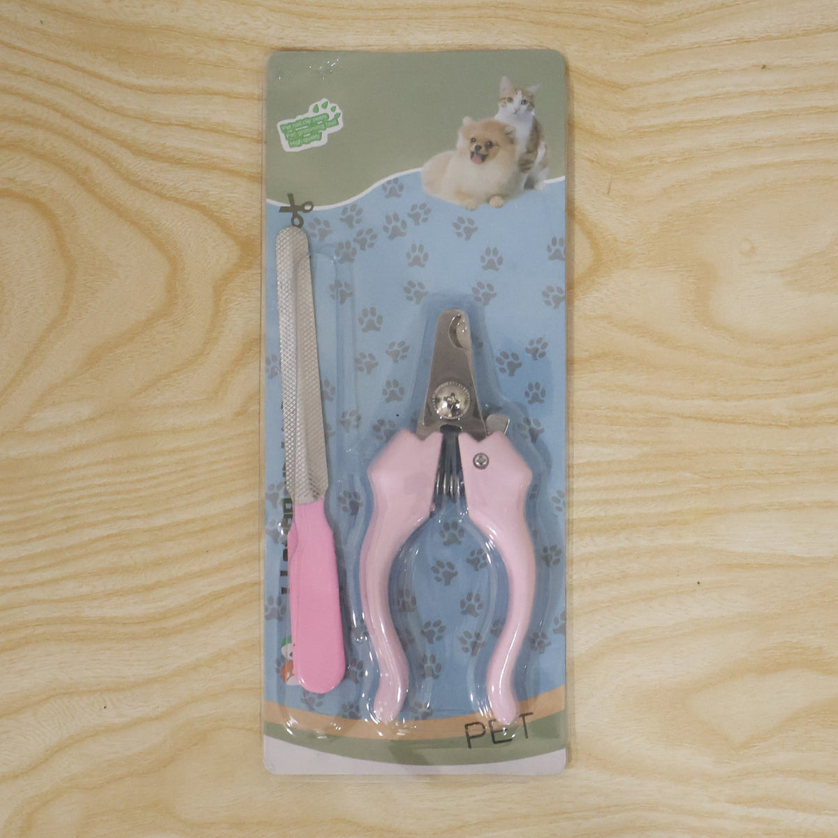 Pink pet nail clipper and filer set in blister packaging on a light wooden background.
