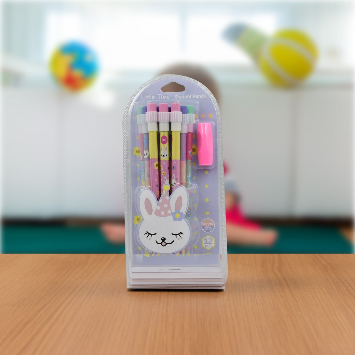 A clear plastic package containing a bunny-themed pencil set, pink eraser, and sharpener stands on a wooden table with a