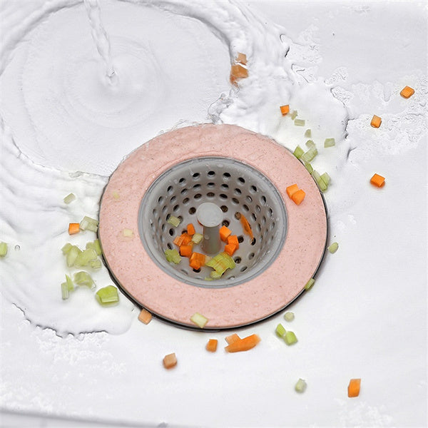 A pink and grey silicone sink strainer basket in a sink with water and chopped vegetables swirling around it.
