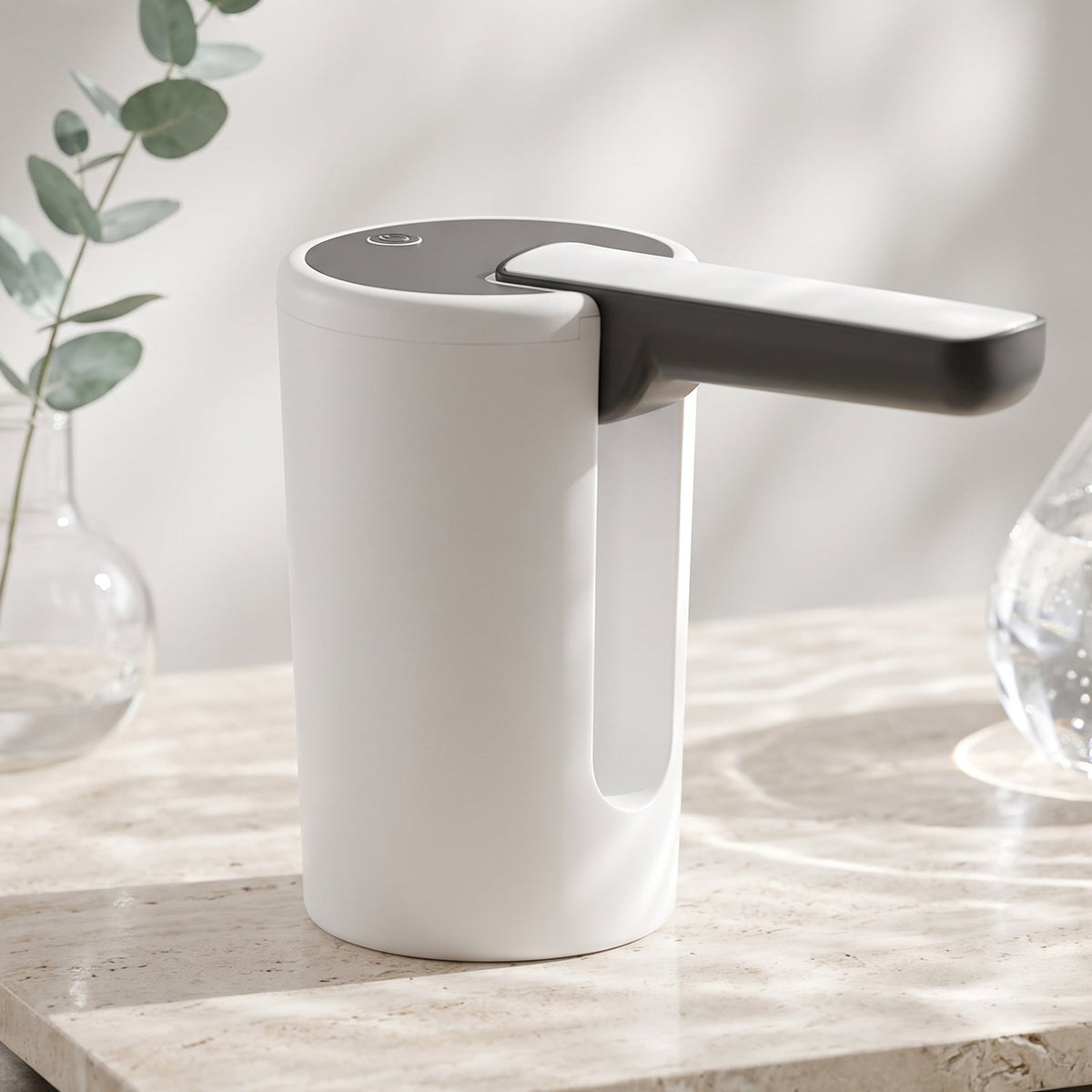 The white and black electric water dispenser pump sits on a marble surface with a glass vase holding eucalyptus branches in