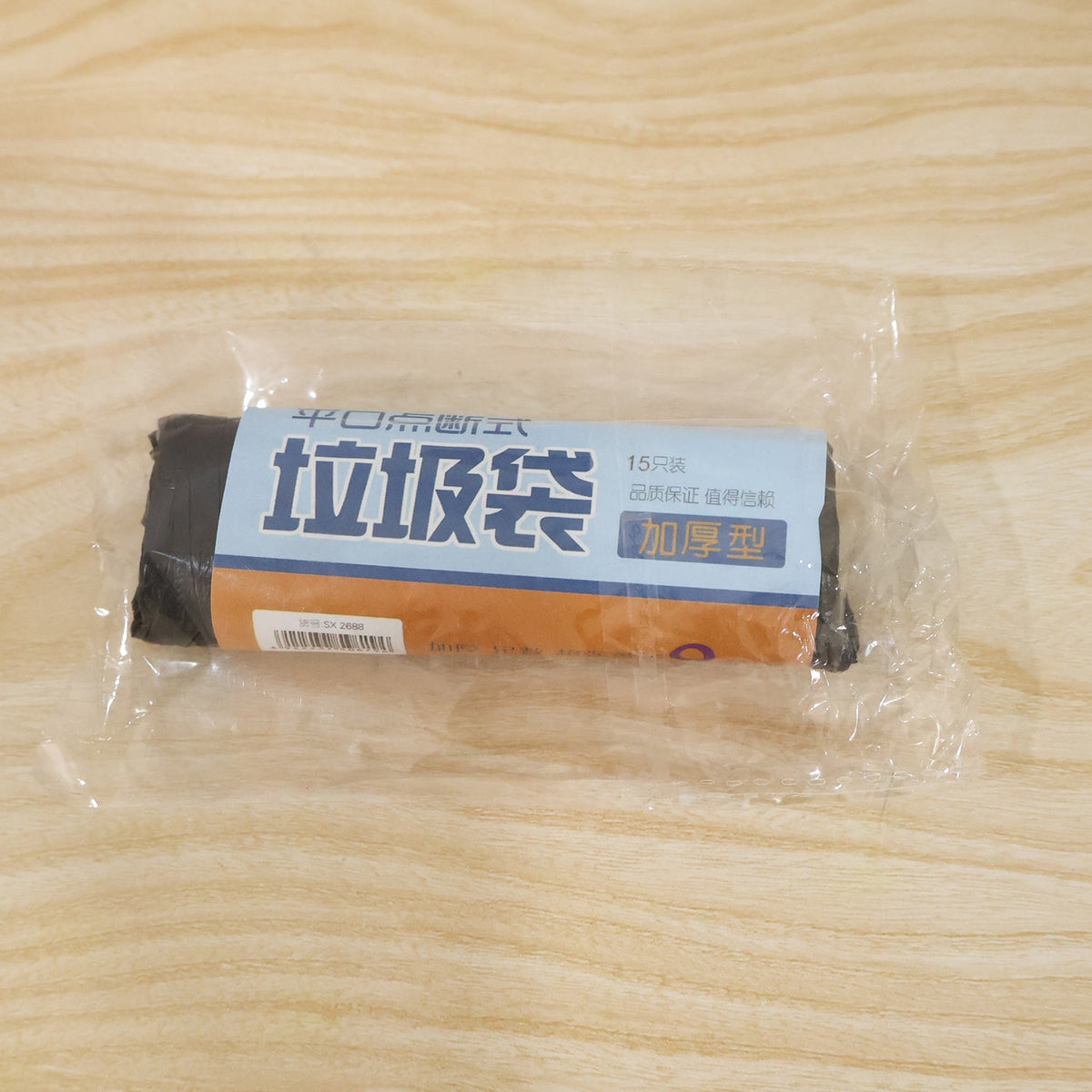 A clear plastic-wrapped roll of black garbage bags with a blue and brown label on a wooden surface.