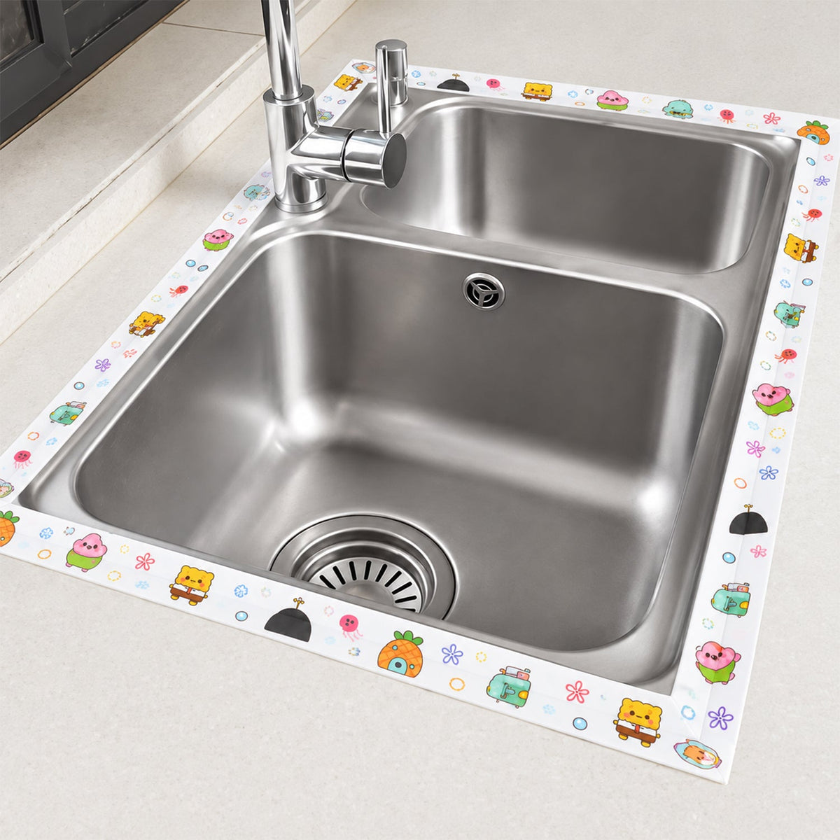 The cartoon-printed sealing tape is applied around the perimeter of a double stainless steel kitchen sink.