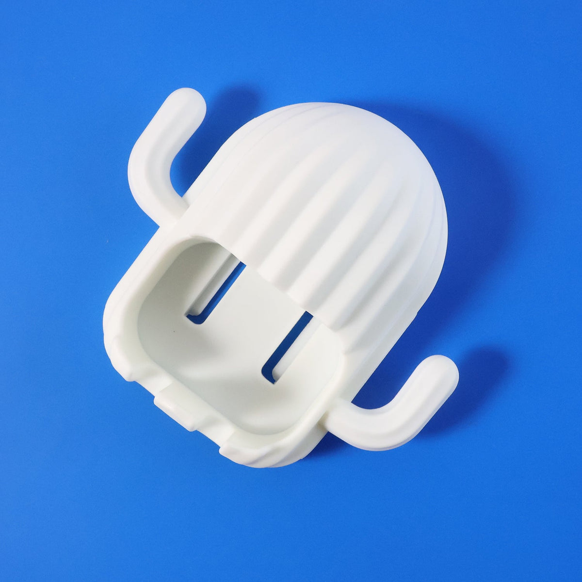 White cactus-shaped toothbrush holder with two slots, positioned diagonally on a vibrant blue background.