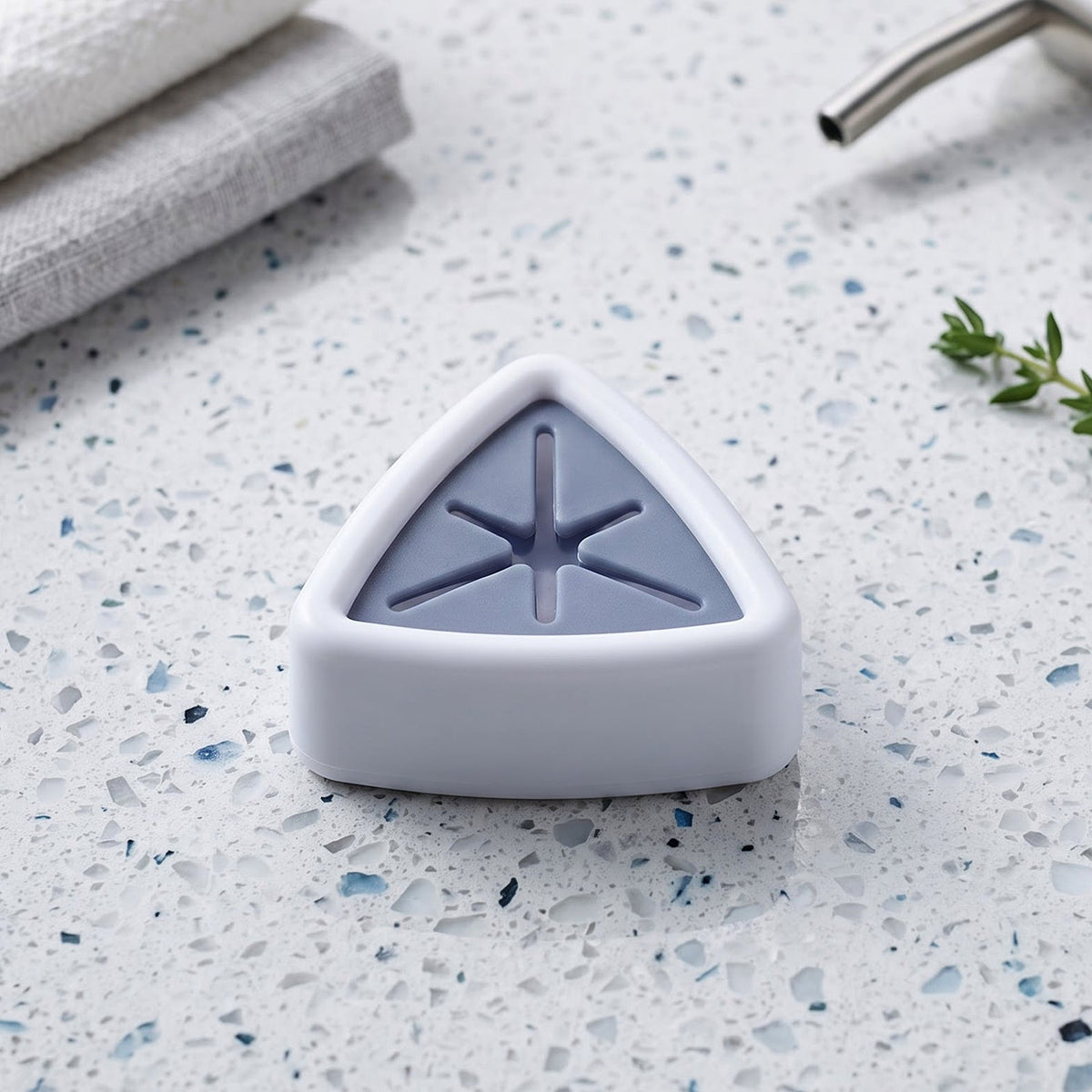 A white and grey triangular towel holder sits on a speckled countertop next to folded white towels and a silver faucet.