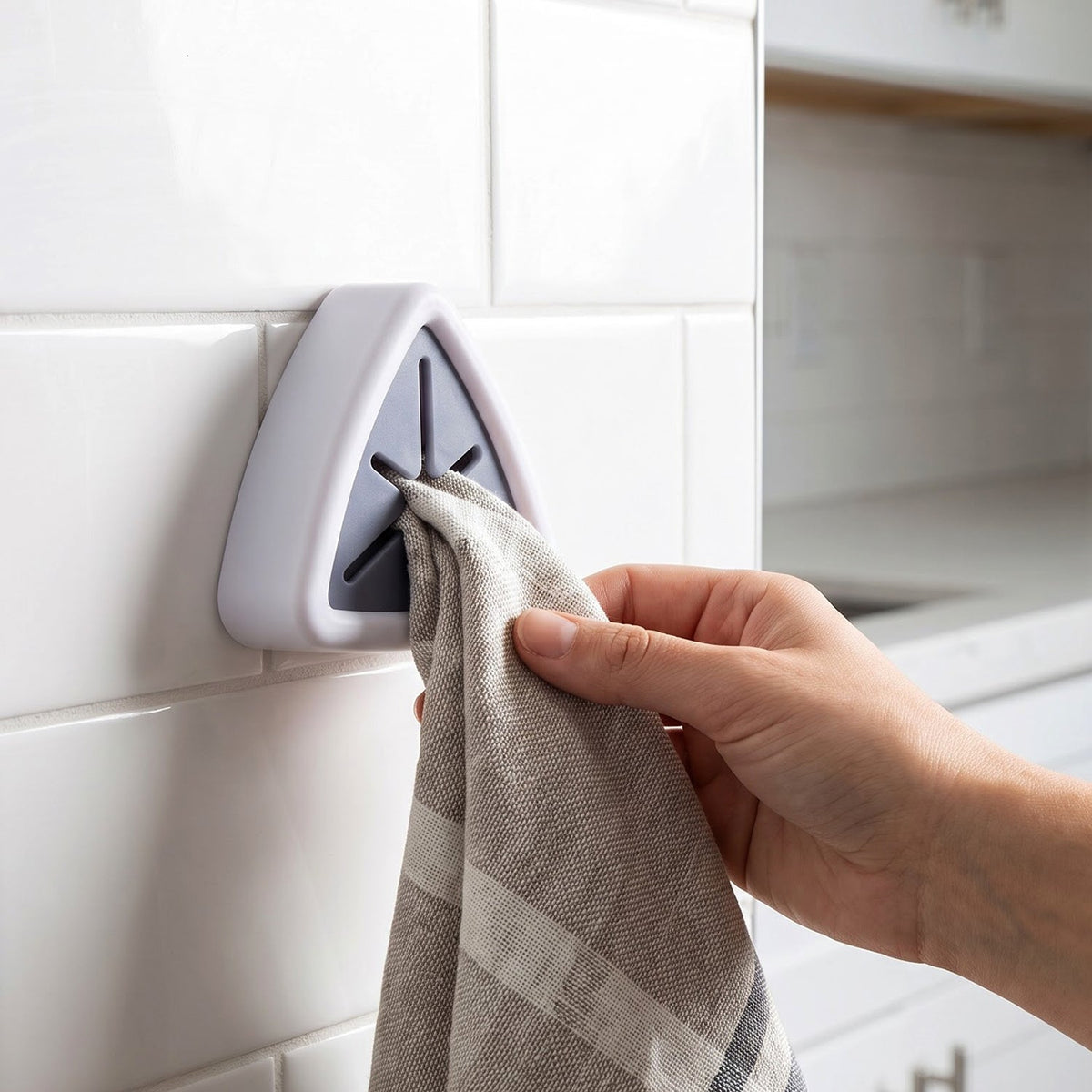 A hand inserts a striped beige towel into a white and grey triangular wall-mounted towel holder on white subway tiles.