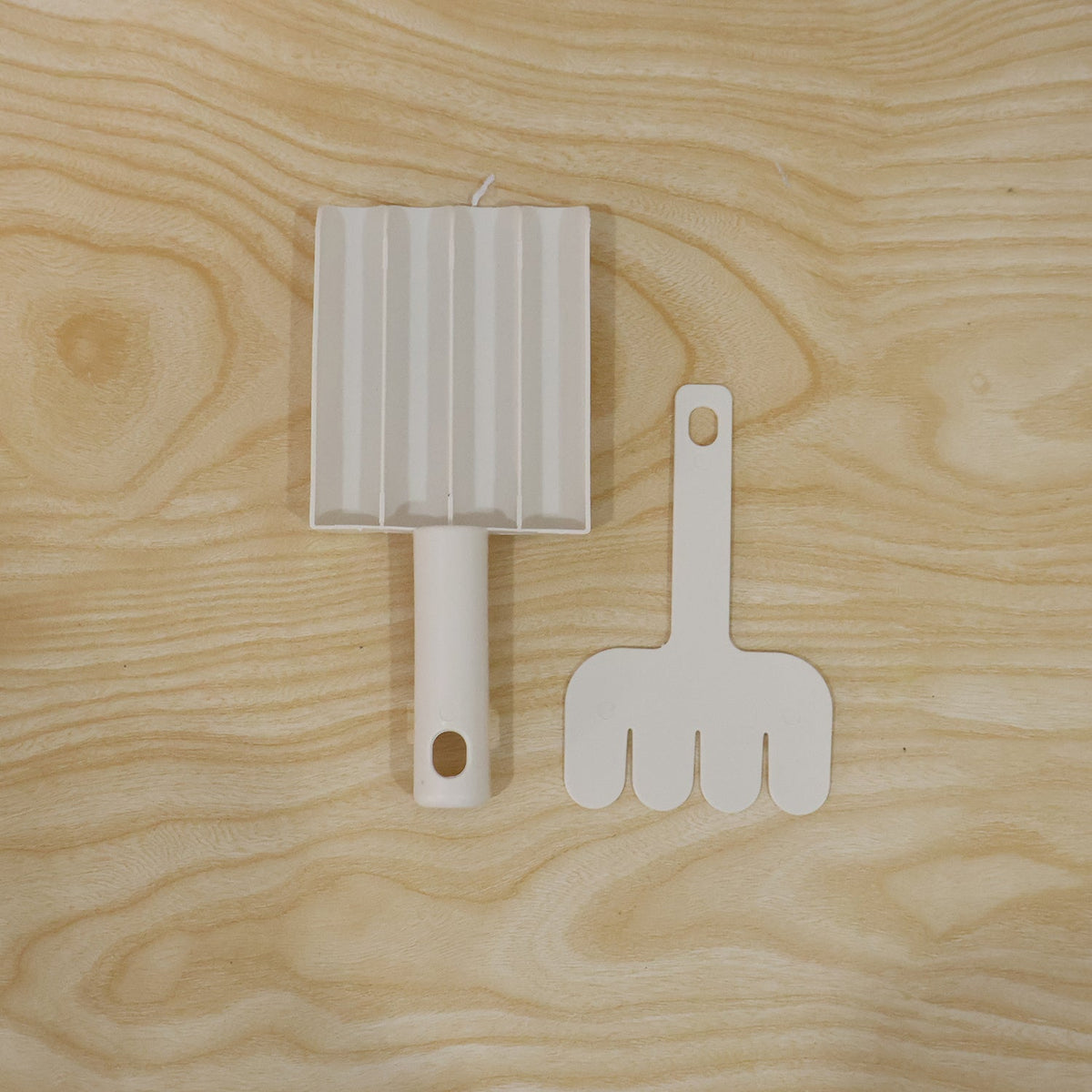 A white plastic meatball maker and a white plastic meatball shaper are displayed on a light wooden surface.