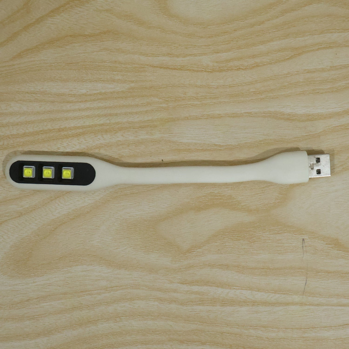 A white flexible USB LED light with three yellow LED bulbs and a USB-A connector resting on a light wood grain surface.