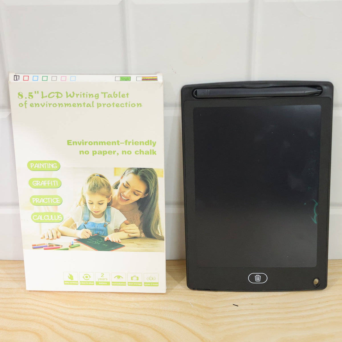 A black LCD writing tablet and its white retail box, featuring an image of a child drawing, are placed side-by-side.