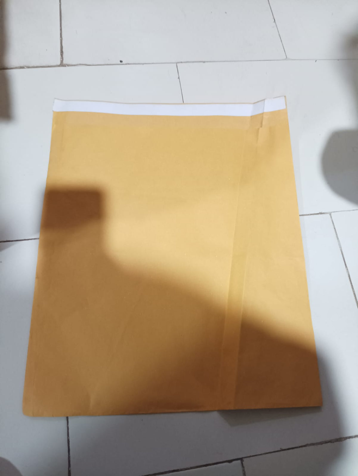 A single brown kraft envelope with a white self-seal strip, lying flat on a tiled floor.